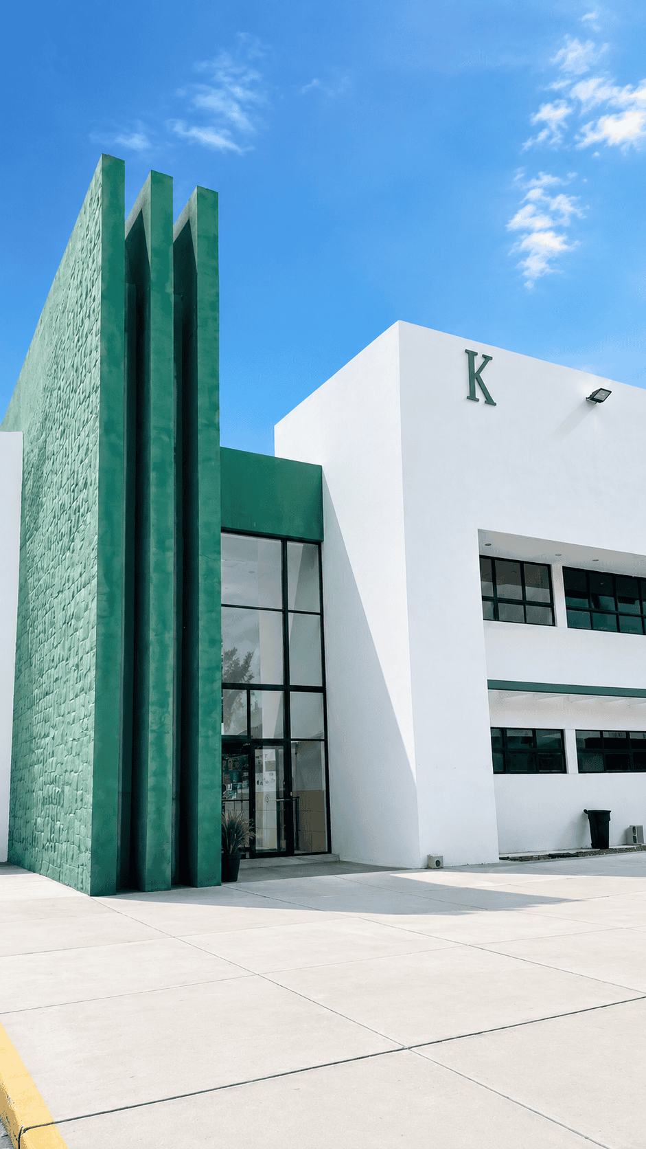 Edificio de arquitectura moderna con paredes verdes y blancas bajo cielo azul.